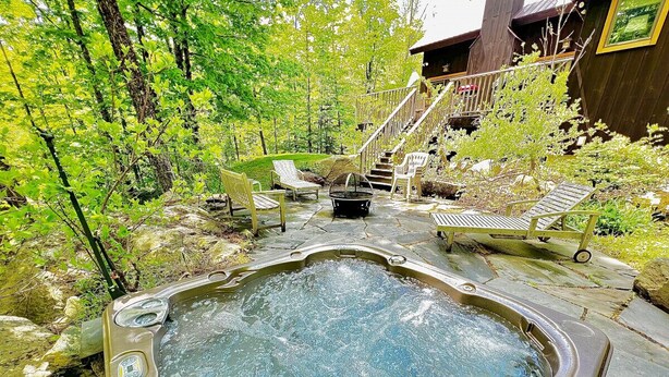 A hot tub surrounded by stone steps, wooden lounge chairs, and a wooden deck. - Your Vermont Mountain Haven Pet Friendly home with Hot tub! (Winhall)