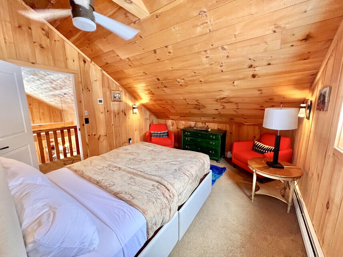 Een gezellig houten slaapkamer met een bed, een rode stoel, een groene dressoir en een kleine tafel met een lamp.