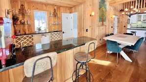 A wooden interior with a kitchen area, bar stools, and a dining table. - Your Vermont Mountain Haven Pet Friendly home with Hot tub! (Winhall)