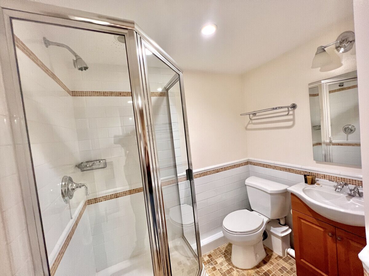 A bathroom with a glass-enclosed shower, a toilet, and a sink with a mirror above.