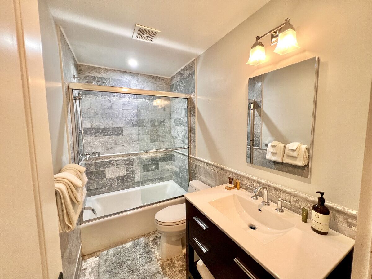 A modern bathroom with a glass-enclosed shower, a bathtub, a toilet, and a vanity with a sink and mirror.