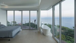 A modern bedroom with a large bed, a bathtub, and a balcony with a view of the sea. - Villa Marina (Playa Ocotal)