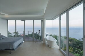 Ein modernes Schlafzimmer mit einem großen Bett, einer Badewanne und einem Balkon mit Meerblick.