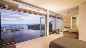 A modern bedroom with a large window overlooking a body of water and hills. - Villa Marina (Playa Ocotal)