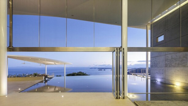 A modern building with a glass facade, an infinity pool, and a view of the ocean. - Villa Marina (Playa Ocotal)
