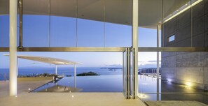 A modern building with a glass facade, an infinity pool, and a view of the ocean.