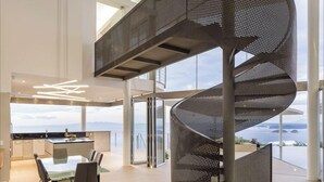 A modern interior with a spiral staircase, a dining area with a glass table, and a view of the sea. - Villa Marina (Playa Ocotal)
