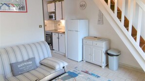 A compact living space with a sofa, a small kitchen area, and a staircase. - Maisonette 3 rooms 4 people 50 m from the port of St Jacques (SARZEAU)