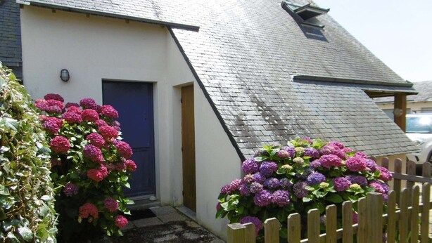 A white house with a blue door, surrounded by a wooden fence and vibrant purple flowers. - Maisonette 3 rooms 4 people 50 m from the port of St Jacques (SARZEAU)