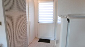 A hallway with a white door, a window with blinds, and a refrigerator. - Maisonette 3 rooms 4 people 50 m from the port of St Jacques (SARZEAU)