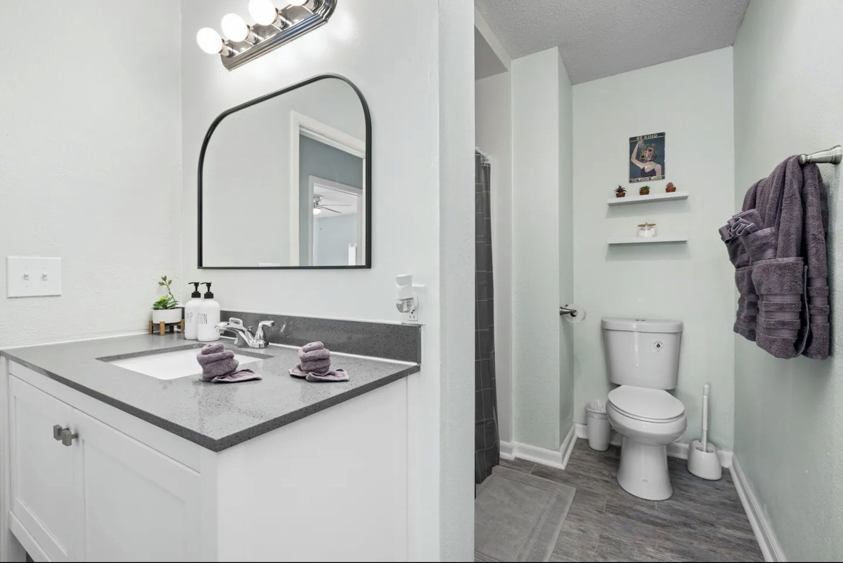 Een badkamer met een wit wastafelmeubel, een grote spiegel met verlichting, een toilet en een douchehoek.