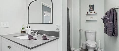 Een badkamer met een wit wastafelmeubel, een grote spiegel met verlichting, een toilet en een douchehoek.
