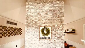 A room with a brick-patterned wall, a welcome sign, a wooden lattice, and a small shelf with a plant. - Cozy and charming private home on an acre lot (Duluth)