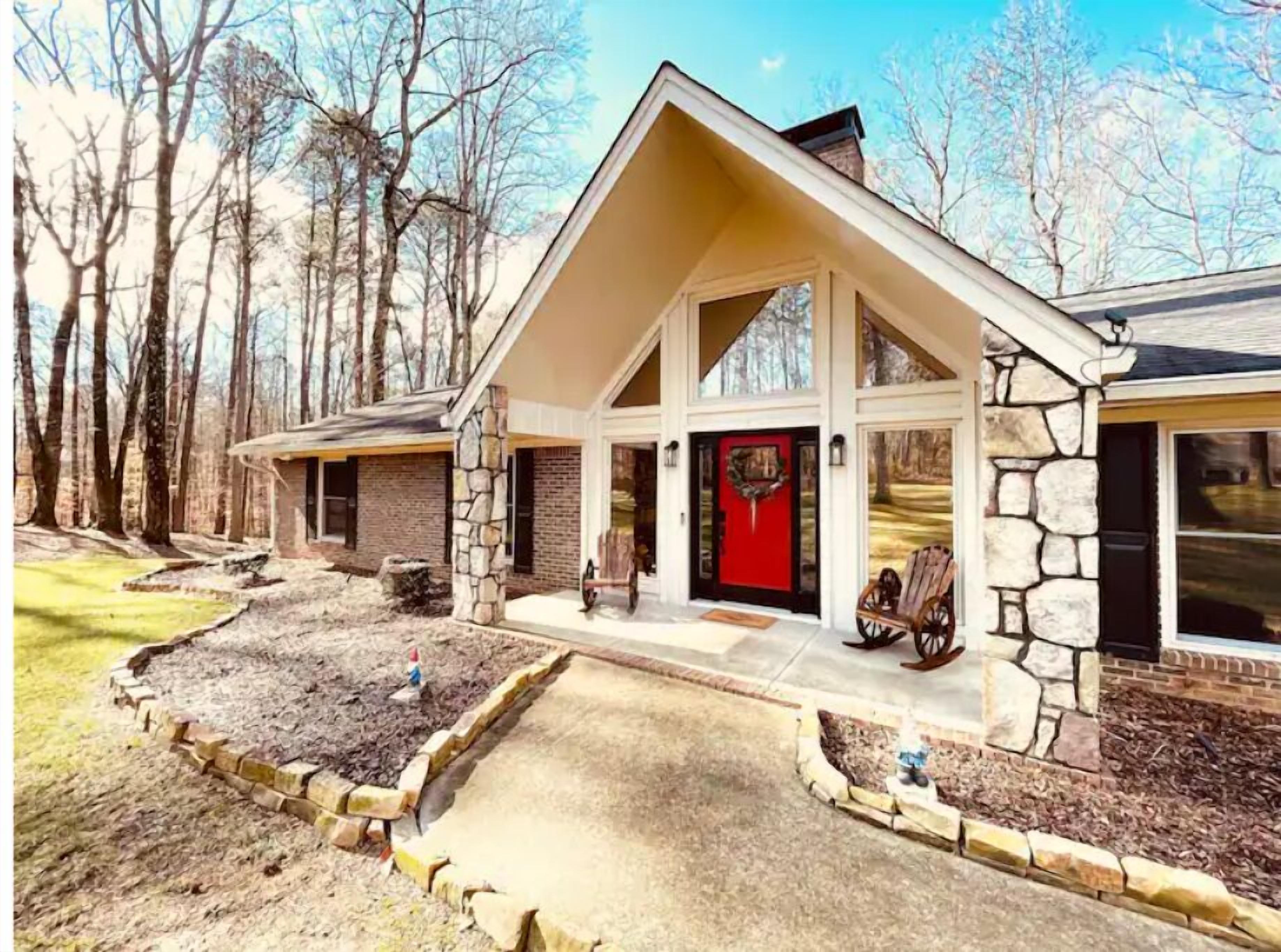 A modern house with a stone facade, a red front door, and a covered porch with a bench.