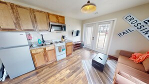 A modern kitchen with wooden cabinets, a microwave, and a stove. There's a dining area with a couch and a rug.