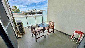 Un balcon avec une table et deux chaises, un petit tabouret et un appareil de climatisation.