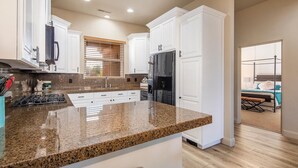 A modern kitchen with white cabinetry, granite countertops, and a wooden floor. - Spacious, Hidden Gem at Point Vista! (St George)