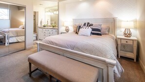 A bedroom with a large bed, bedside tables, a bench, a mirror, and a bathroom with a sink and mirror. - Spacious, Hidden Gem at Point Vista! (St George)