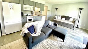 Un espacio habitable pequeño con kitchenette, un sofá gris y una lámpara de pie.