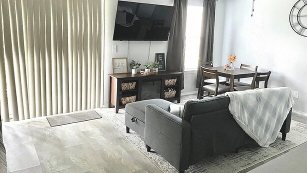 Una sala de estar con un sofá, una mesa de centro, un televisor y una mesa de comedor con sillas.