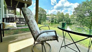 Un patio con una silla y una mesa, con vistas a un área verde con árboles y un edificio al fondo.