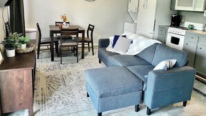 Un espacio habitable compacto con comedor, kitchenette y un sofá gris.