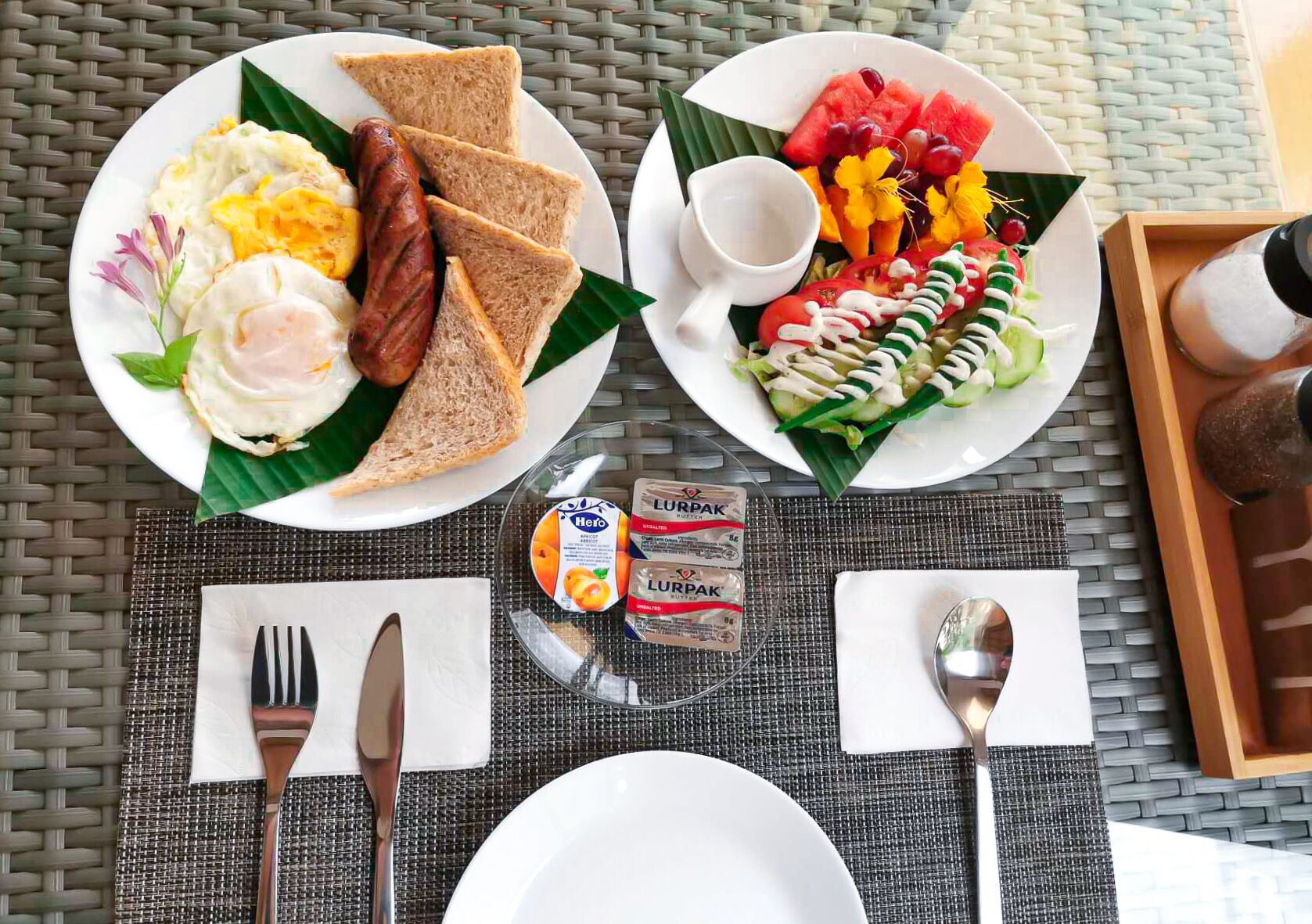 Un desayuno con dos platos de comida, una servilleta, cubiertos y un pequeño recipiente con yogur.