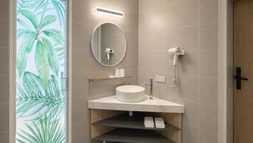 Un baño moderno con un espejo redondo, un lavabo blanco y un secador de pelo fijado a la pared.