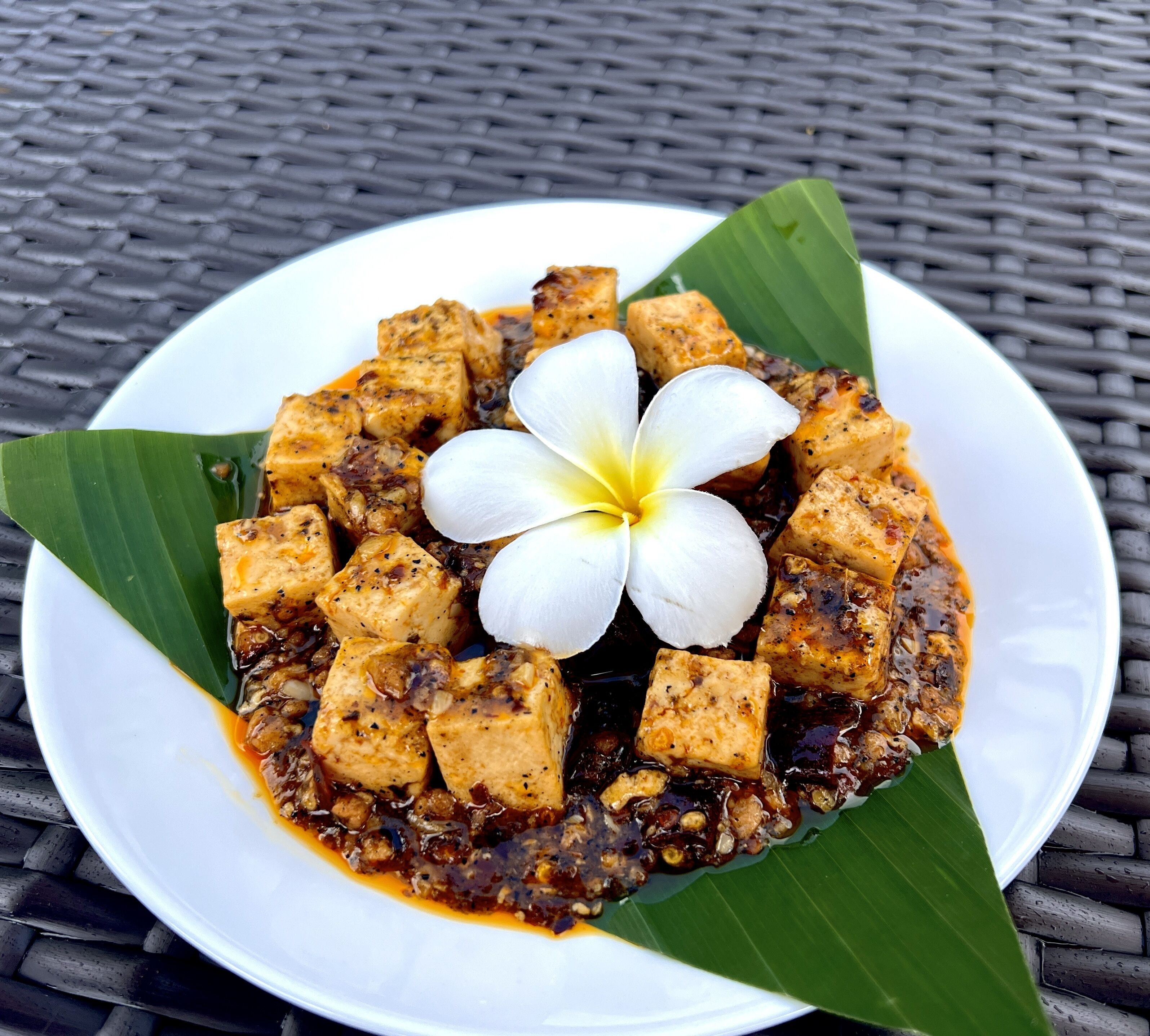 Un piatto di tofu guarnito con un fiore su un tavolo intrecciato.