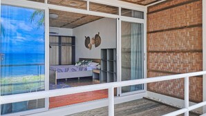 A room with a large sliding glass door leading to a balcony, a bed with a view of the sea, and a woven ceiling. - Blue Joys Marine Sports Resort (San Juan)