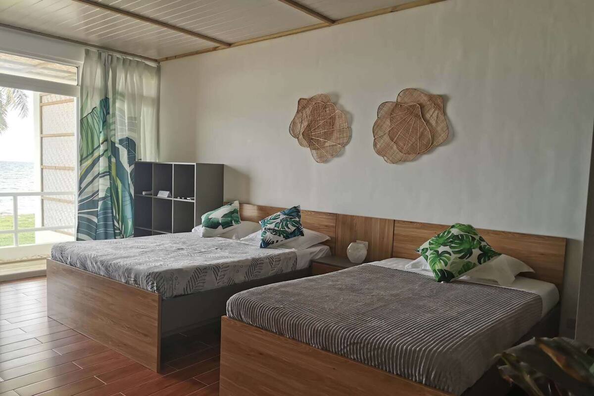 Ein Hotelzimmer mit zwei Betten, Holzboden, einem großen Fenster mit Vorhängen und Wanddekoration.
