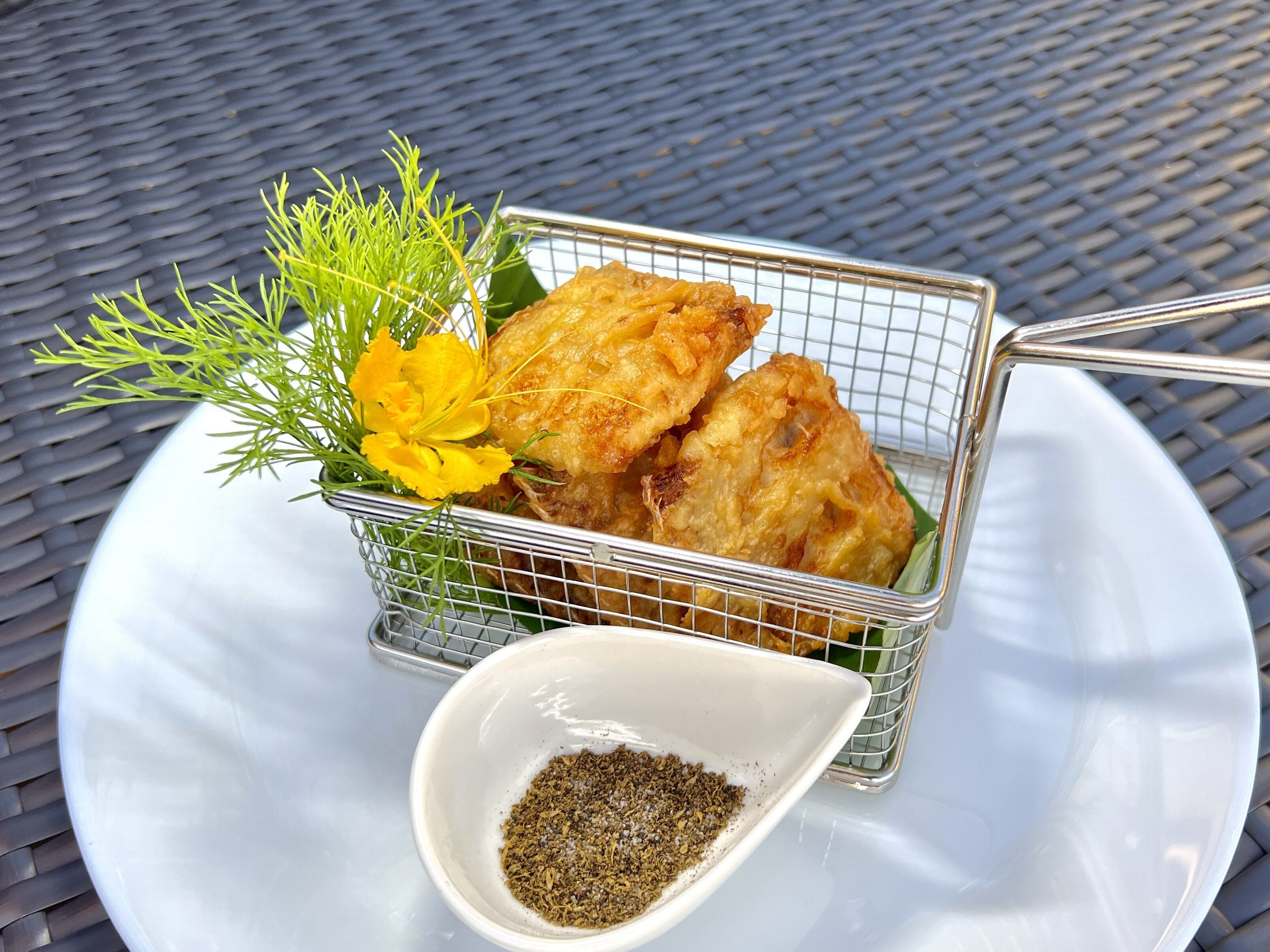 Una cesta de comida frita con un recipiente pequeño de especias sobre un plato blanco.