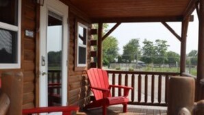 A wooden deck with red Adirondack chairs and a table, overlooking a grassy area. - Cozy cabin with views of Lake Erie and colorful sunsets! (Ashtabula)