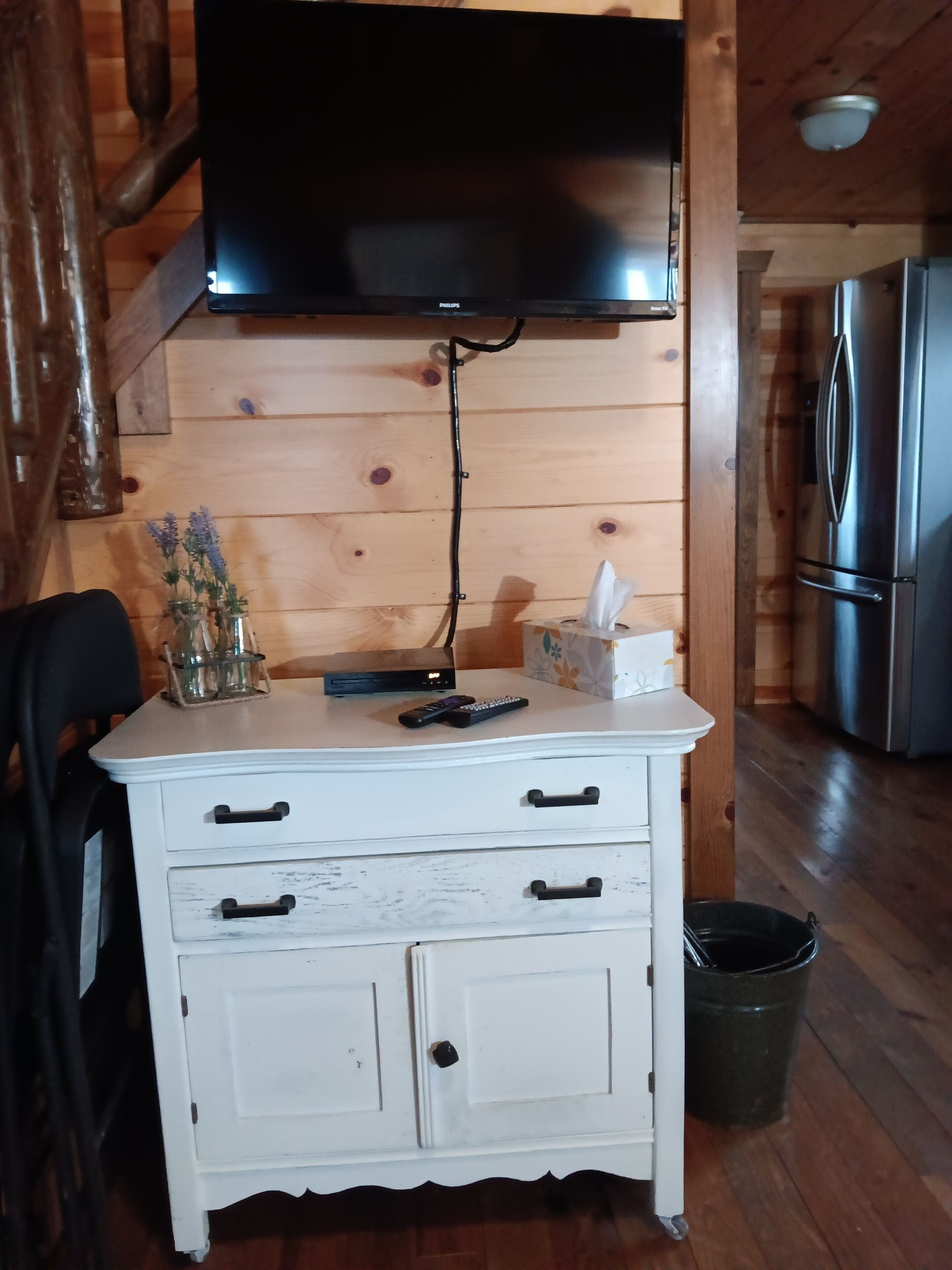 A wooden interior with a white cabinet, a flat-screen TV mounted on the wall, a remote control, a tissue box, and a trash can.