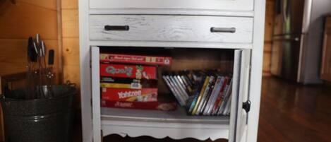 A white cabinet with two drawers and a shelf containing books and a box labeled "Yachtzee."