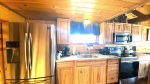 A wooden cabin-style kitchen with a stainless steel refrigerator, a microwave, a stove, and wooden cabinets. - Cozy cabin with views of Lake Erie and colorful sunsets! (Ashtabula)