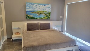 Un dormitorio con una cama, dos almohadas, una mesita de noche, un cuadro y una ventana con persianas.