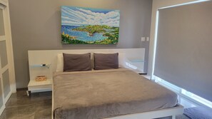 Ein Schlafzimmer mit einem Bett, zwei Kissen, einem Nachttisch, einem Gemälde und einem Fenster mit Jalousien.