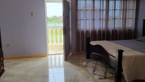 Quarto com cama, porta para varanda e vista para o exterior.