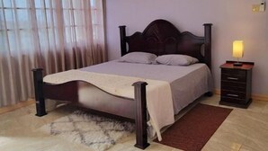 Quarto com cama, mesa de cabeceira, luminária, janela com cortinas e luz no teto.