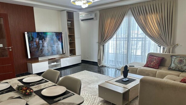 A modern living room with a dining area, a flat-screen TV, and a sofa with decorative pillows. - RESIDENCE DIBA ALMADIES NGOR (Dakar)