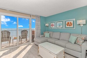 A living room with a sofa, chairs, a coffee table, and a balcony with a view.