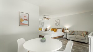 Ein modernes Hotelzimmer mit einem runden Esstisch, einer Couch und einem Bett mit gelben Kissen.