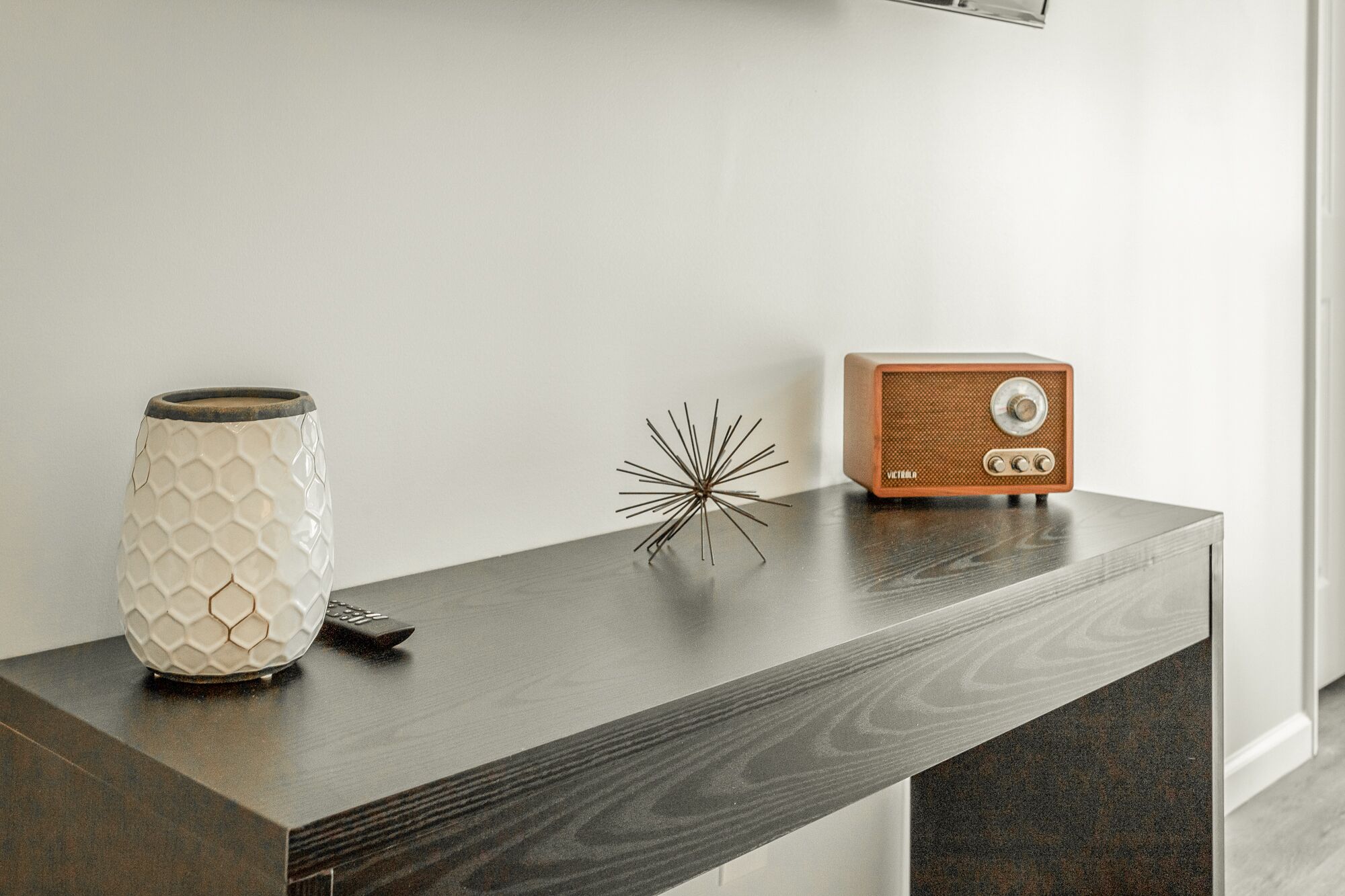 A wooden console table with a white ceramic vase, a decorative metal piece, and a vintage radio.