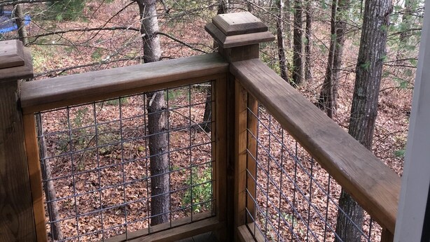 A wooden deck with a metal railing overlooking a forested area.