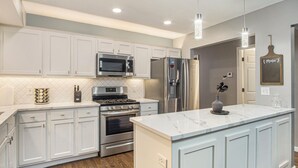 A modern kitchen with white cabinetry, stainless steel appliances, and a marble island. -  Modern 4BR Near Downtown, Chef Kitchen, Fenced Yard, EV Charger, W/D (Omaha)