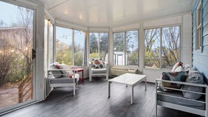 A sunroom with a large glass door, a white sofa, a white chair, and a small table. -  Modern 4BR Near Downtown, Chef Kitchen, Fenced Yard, EV Charger, W/D (Omaha)