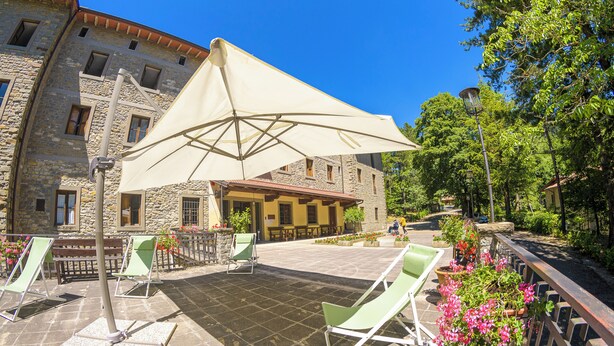 A courtyard with stone flooring, outdoor seating, and a large umbrella providing shade. - Pastor Angelicus - Casa per Ferie (Chiusi della Verna)