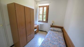 Une petite chambre avec une armoire en bois, un lit simple, une table de chevet et une fenêtre avec des rideaux.