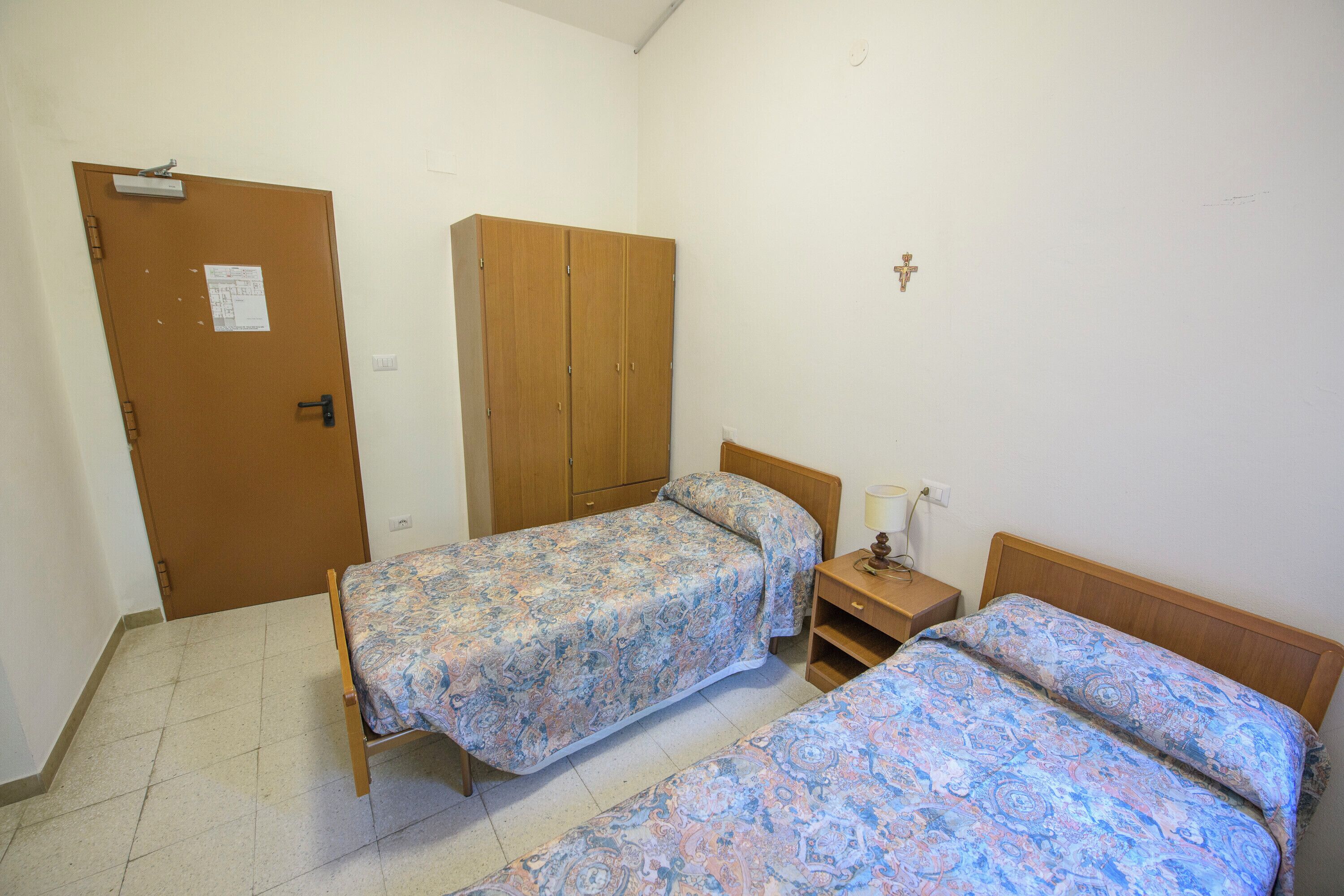 Un dormitorio con dos camas individuales, un armario de madera, una puerta con un aviso y una lámpara fijada a la pared.